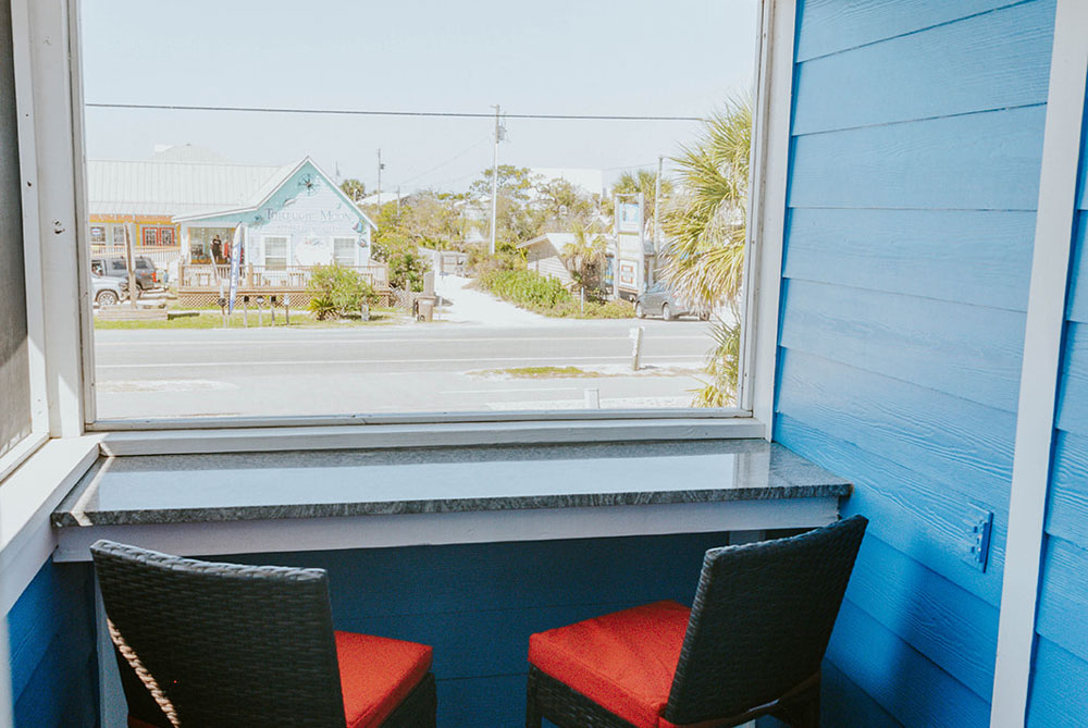 View from the blue-walled porch of a Cape San Blas inn, featuring a stone counter and two chairs facing a coastal street and storefronts.