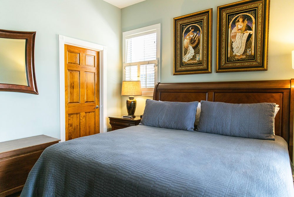 A bedroom at the Cape San Blas Inn featuring a bed with a blue quilt and two framed prints of Art Nouveau-style women hanging on the wall above the headboard.