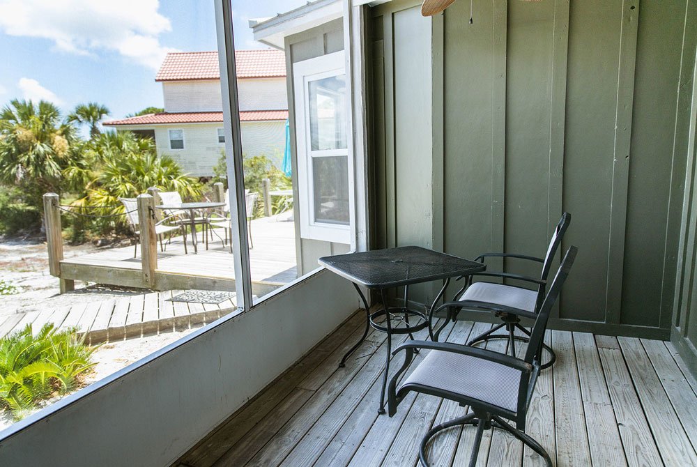 A screened-in scallop shell room at the Cape San Blas Inn featuring a metal table and two chairs, overlooking a deck and nearby coastal vegetation.