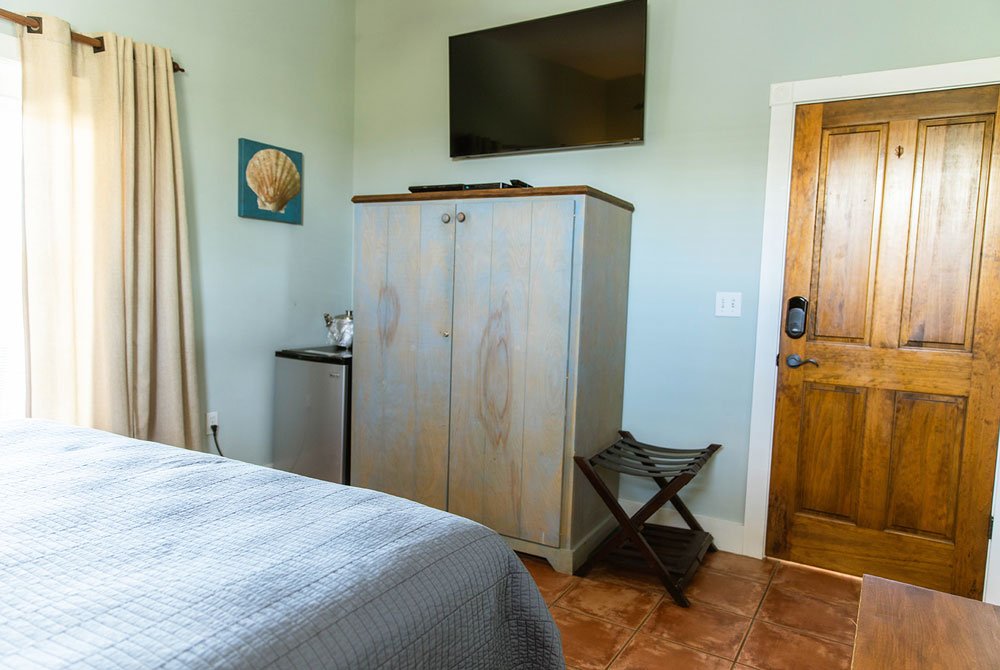 A bedroom at the Scallop Shell Inn featuring a blue wooden cabinet, a wall-mounted television, a small refrigerator, and a wooden door.