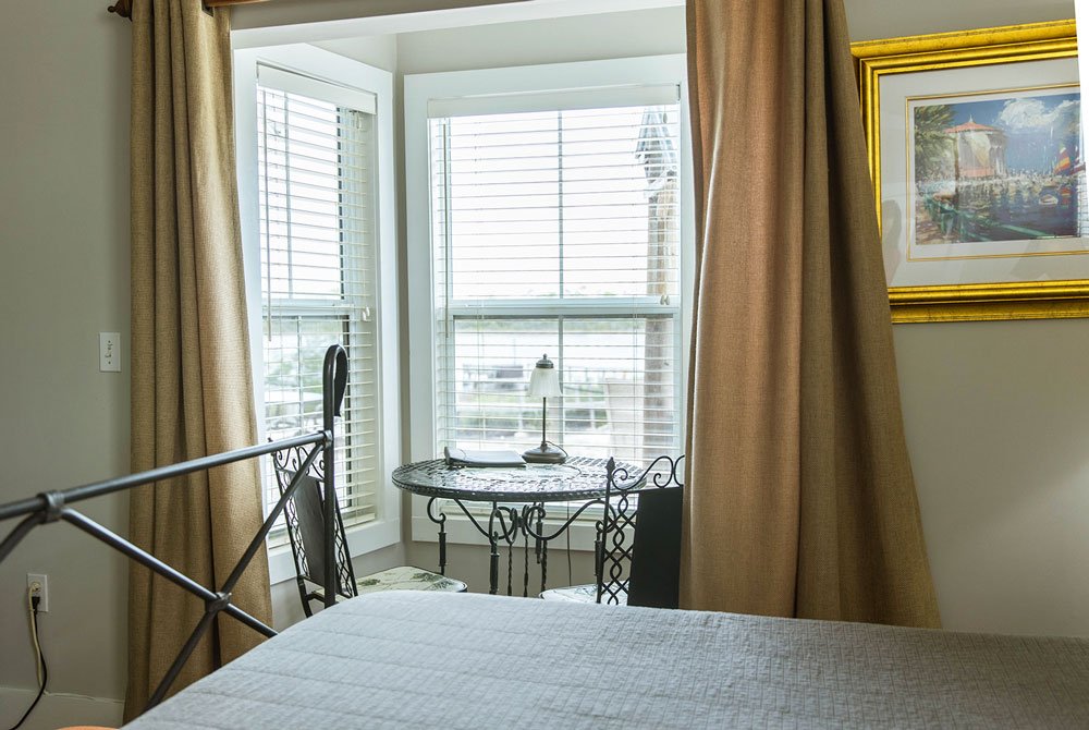 A metal bistro table and two chairs positioned by a window in a Conch Shell Room at the Cape San Blas Inn, overlooking a body of water.