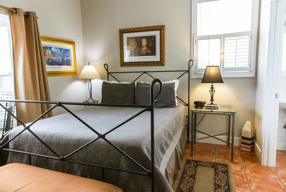 A queen-sized bed with a dark metal frame and grey bedding, flanked by two nightstands with lamps and framed artwork, in a room at the Cape San Blas Inn.