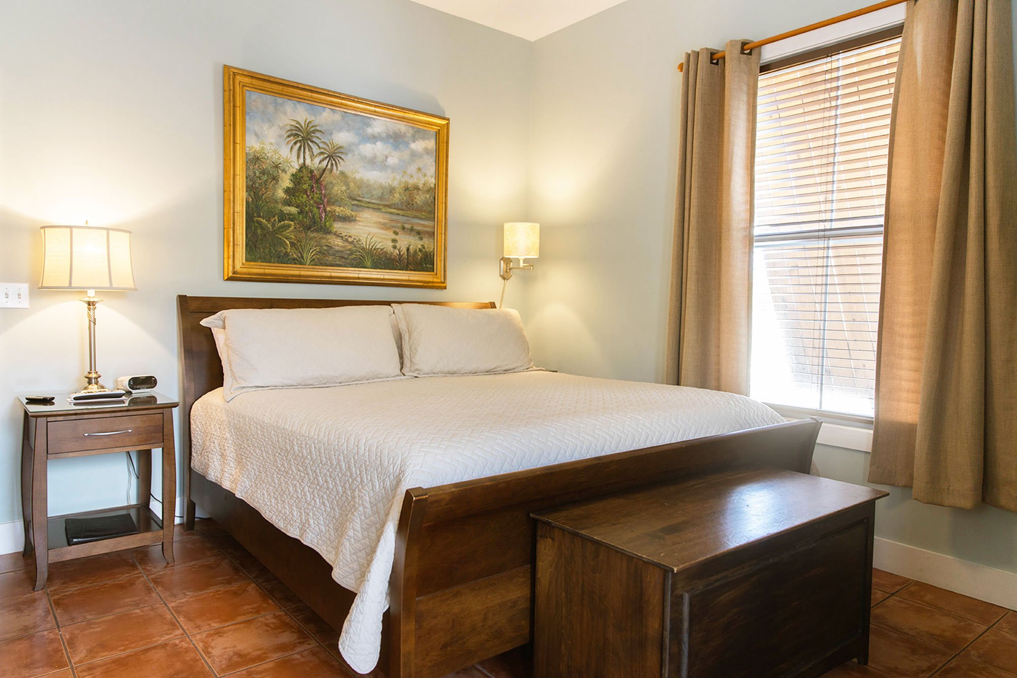 A bedroom at the oyster shell room featuring a wooden sleigh bed, a landscape painting above the headboard, and a bedside table with a lamp.