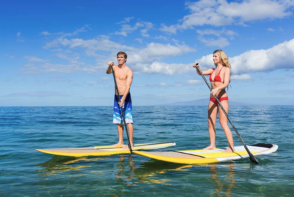 A man and a woman stand on separate paddleboards in the ocean, a popular choice for things to do in Port St. Joe, Florida, as they use paddles to move through the water.