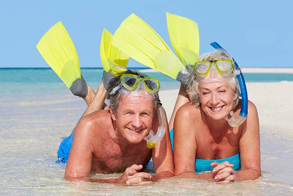 A smiling couple wearing snorkel gear and flippers lying in the shallow surf on a beach, enjoying popular things to do in Port St. Joe, Florida.